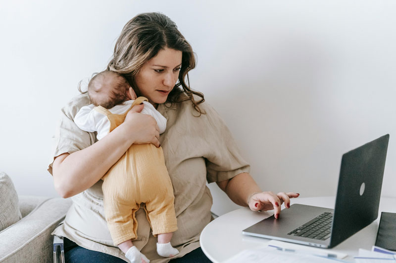 a nursing mother carrying her baby and using a laptop at the same time.
